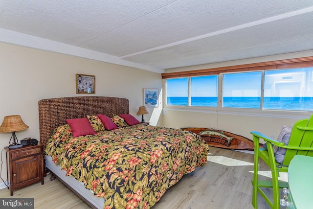 bedroom with a textured ceiling, a water view, and wood finished floors