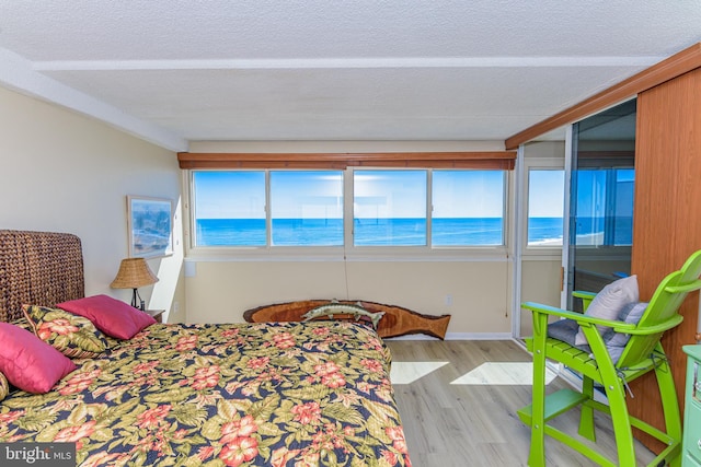 bedroom featuring baseboards, light wood-type flooring, a water view, and a textured ceiling