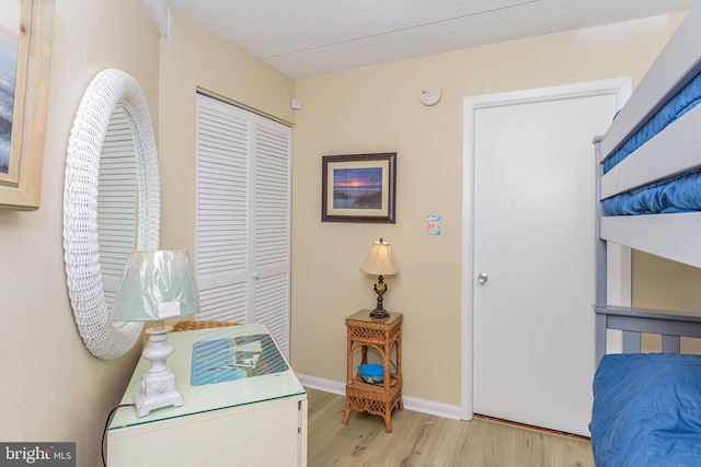 bedroom with a textured ceiling, wood finished floors, a closet, and baseboards