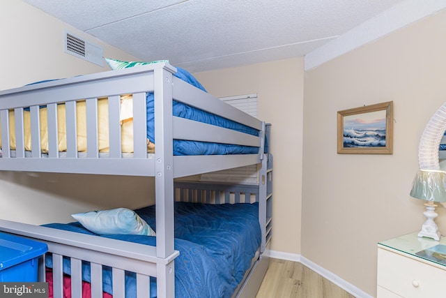 bedroom featuring visible vents, baseboards, a textured ceiling, and wood finished floors