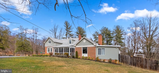 view of front of home featuring brick siding, fence, a front yard, a chimney, and a sunroom