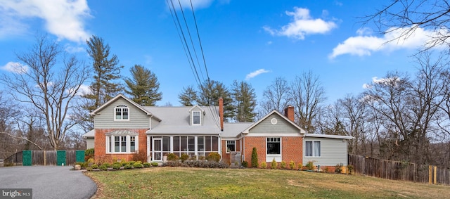 traditional home featuring a front lawn, fence, brick siding, and a sunroom