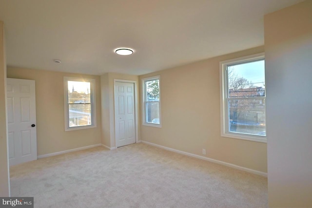 unfurnished bedroom featuring multiple windows, light colored carpet, and baseboards