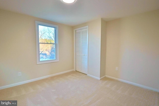 unfurnished bedroom with a closet, light colored carpet, and baseboards