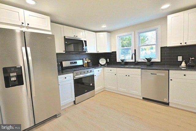 kitchen with a sink, dark countertops, appliances with stainless steel finishes, and light wood-style flooring