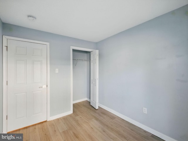 unfurnished bedroom featuring light wood finished floors, a closet, and baseboards