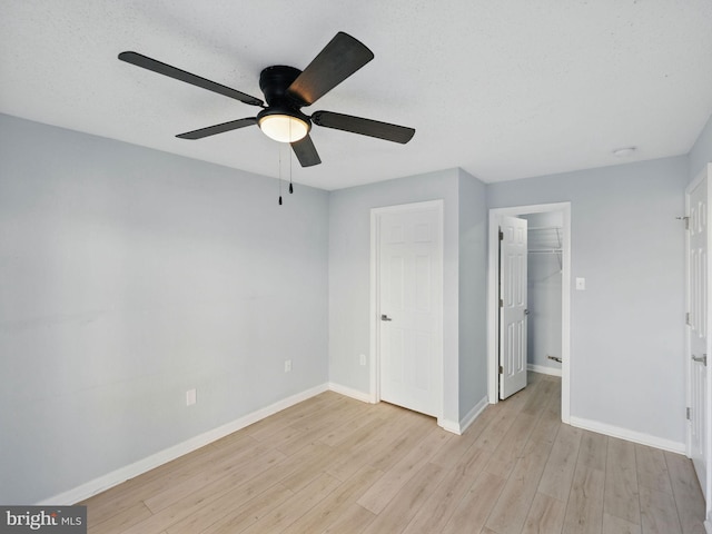 unfurnished bedroom with a spacious closet, ceiling fan, baseboards, light wood-style floors, and a closet