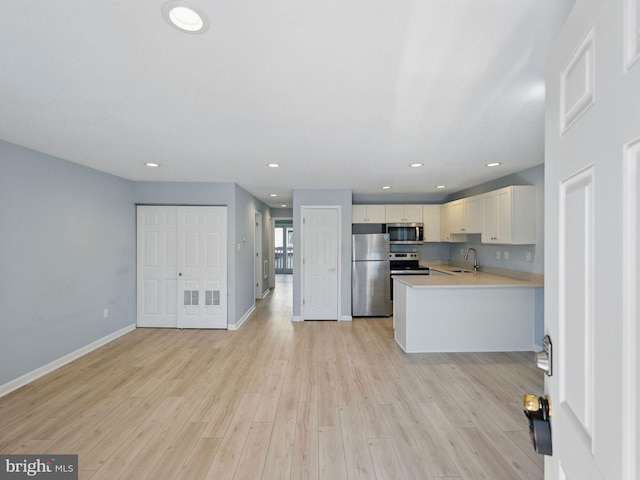 kitchen featuring baseboards, light wood finished floors, stainless steel appliances, a sink, and light countertops