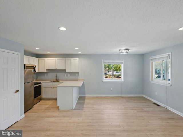 kitchen featuring a peninsula, stainless steel appliances, a sink, light countertops, and light wood-type flooring