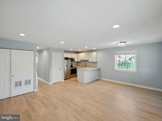 kitchen featuring open floor plan, light wood-style floors, a peninsula, appliances with stainless steel finishes, and light countertops