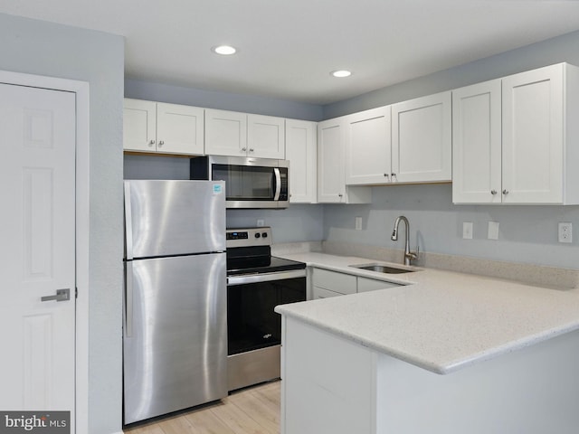 kitchen with a peninsula, light wood-style flooring, a sink, appliances with stainless steel finishes, and white cabinetry