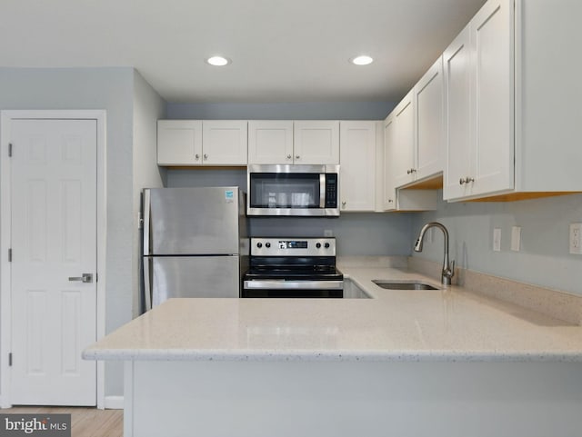 kitchen with white cabinetry, light stone countertops, stainless steel appliances, and a sink