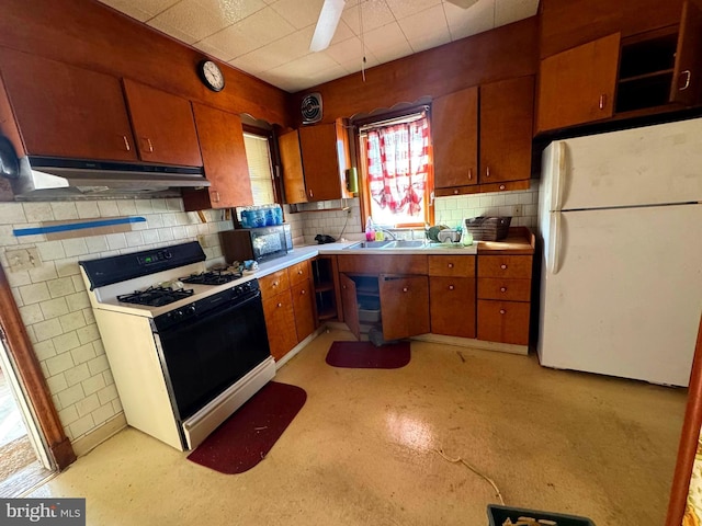 kitchen with under cabinet range hood, range with gas cooktop, brown cabinetry, and freestanding refrigerator