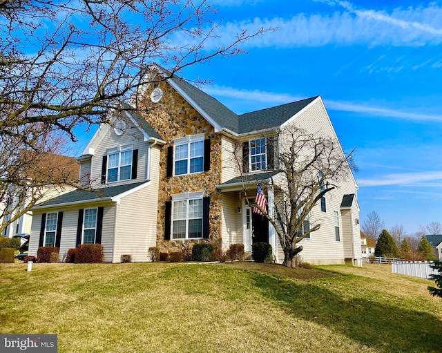 traditional-style house featuring stone siding, a front yard, and fence