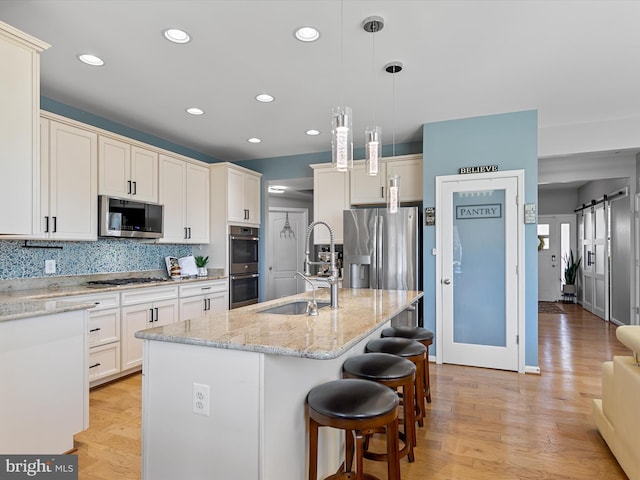 kitchen with light wood-style flooring, appliances with stainless steel finishes, a barn door, and a sink