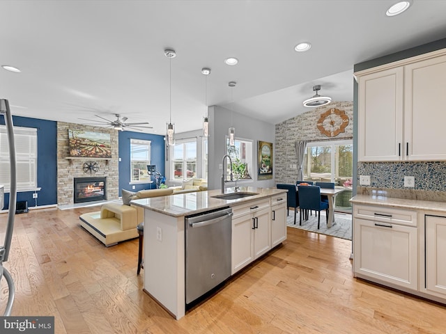 kitchen with light wood-style floors, lofted ceiling, stainless steel dishwasher, and a fireplace