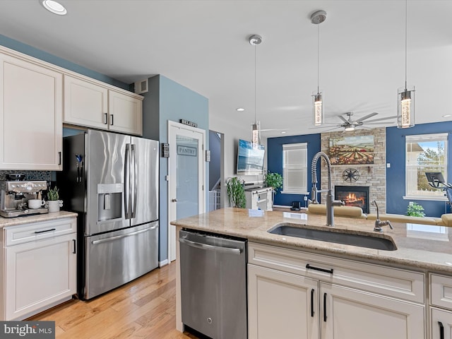 kitchen featuring a sink, open floor plan, white cabinetry, stainless steel appliances, and a large fireplace