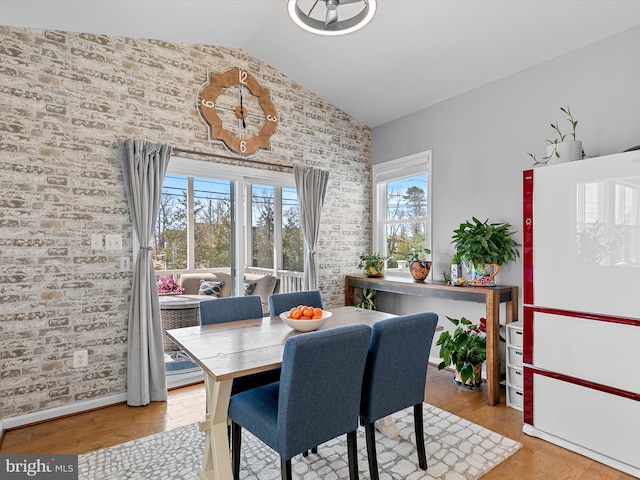 dining space featuring baseboards, wood finished floors, brick wall, and vaulted ceiling