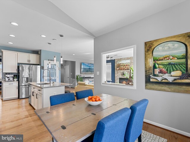 dining space with light wood finished floors, baseboards, lofted ceiling, recessed lighting, and a glass covered fireplace