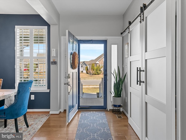 foyer entrance featuring light wood-type flooring, a barn door, and baseboards