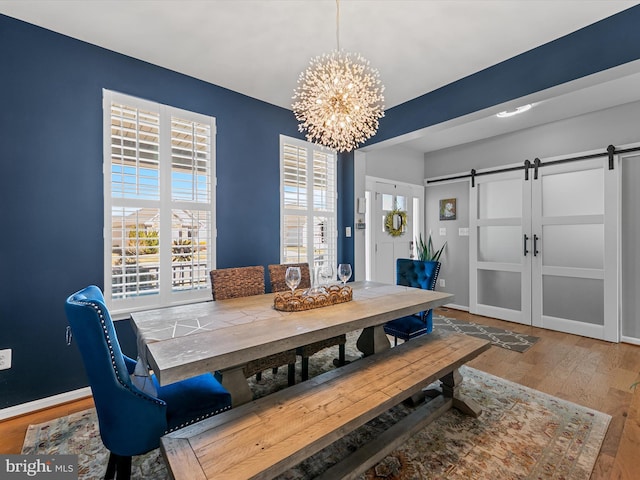 dining area featuring a barn door, a notable chandelier, wood finished floors, and baseboards