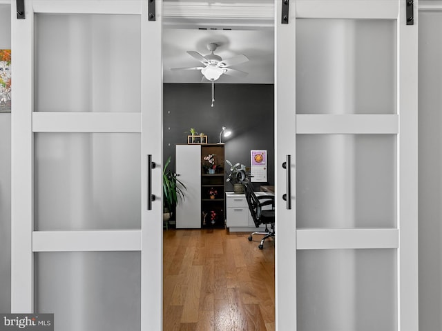 home office with a ceiling fan, a barn door, and wood finished floors