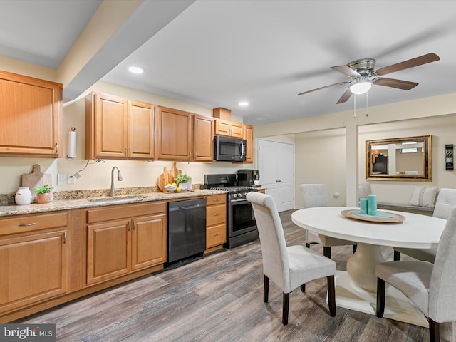 kitchen featuring stainless steel range with gas stovetop, dishwasher, light stone counters, wood finished floors, and a sink