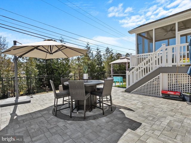 view of patio with stairway, outdoor dining area, fence, and a sunroom