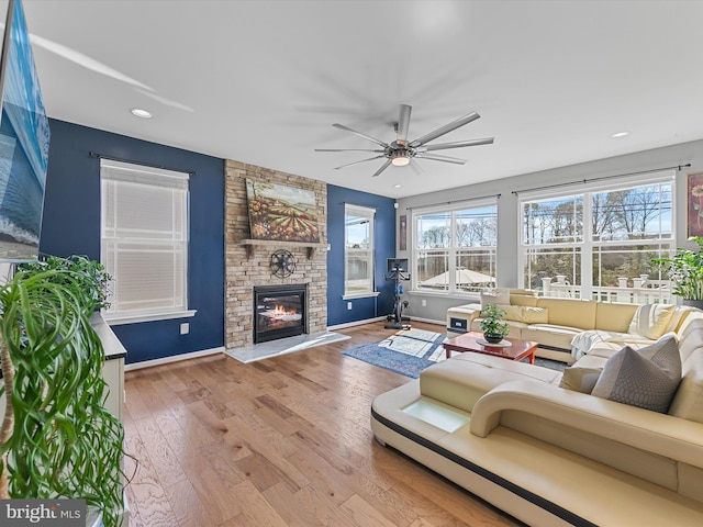 living area featuring wood finished floors, baseboards, recessed lighting, ceiling fan, and a stone fireplace