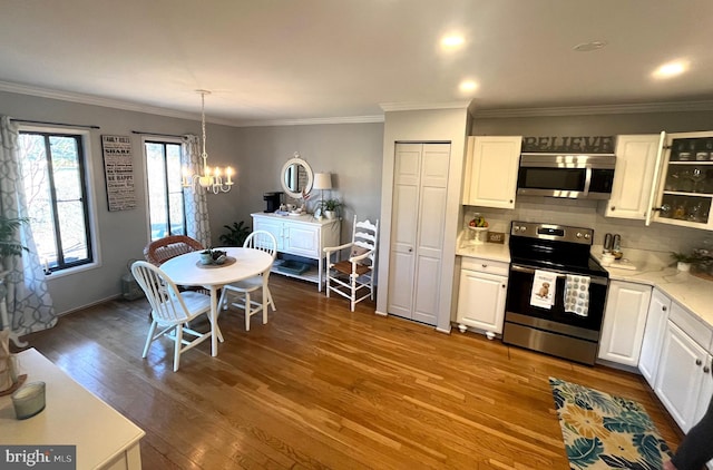 kitchen featuring decorative backsplash, an inviting chandelier, wood finished floors, white cabinets, and stainless steel appliances