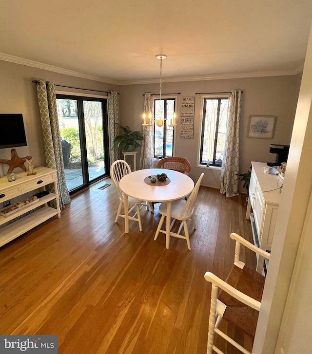 dining space featuring a healthy amount of sunlight, ornamental molding, an inviting chandelier, and wood finished floors