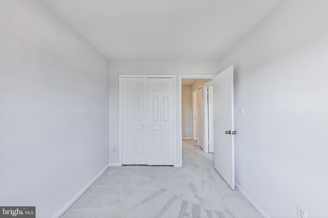 unfurnished bedroom featuring a closet, baseboards, and light colored carpet