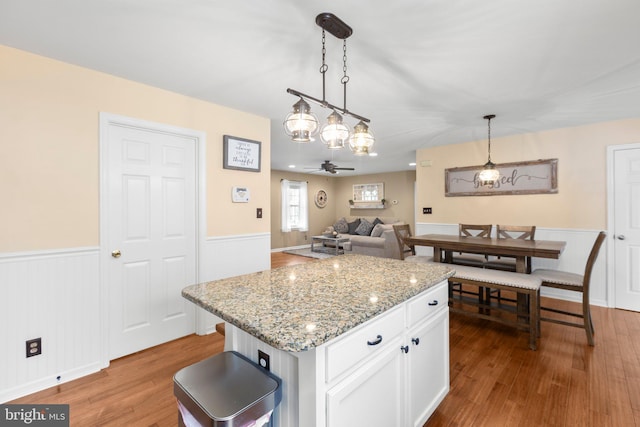 kitchen with a wainscoted wall, a ceiling fan, decorative light fixtures, wood finished floors, and white cabinets