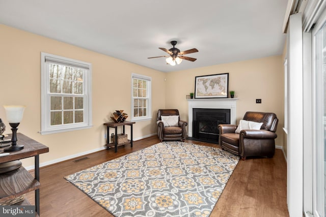 sitting room featuring visible vents, a fireplace with flush hearth, a ceiling fan, wood finished floors, and baseboards