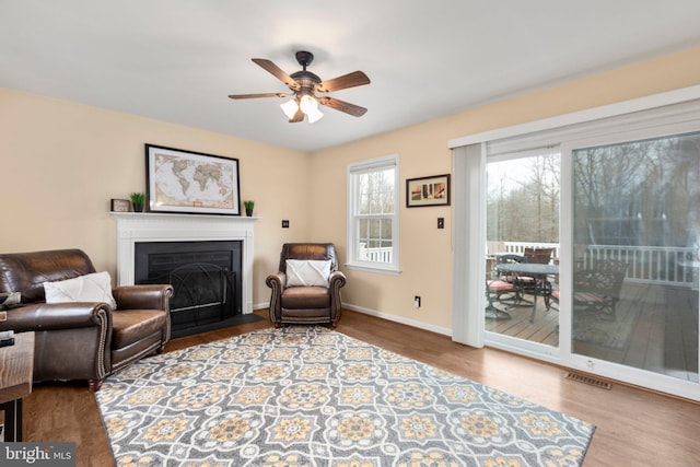 sitting room featuring visible vents, baseboards, ceiling fan, a fireplace with flush hearth, and wood finished floors