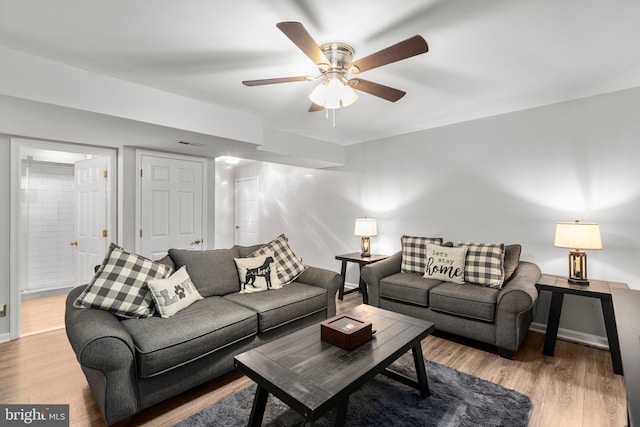 living room featuring a ceiling fan, wood finished floors, visible vents, and baseboards