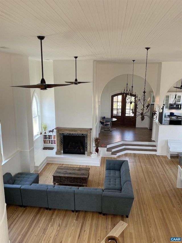 living room featuring a fireplace with raised hearth, ceiling fan, lofted ceiling, wood finished floors, and arched walkways