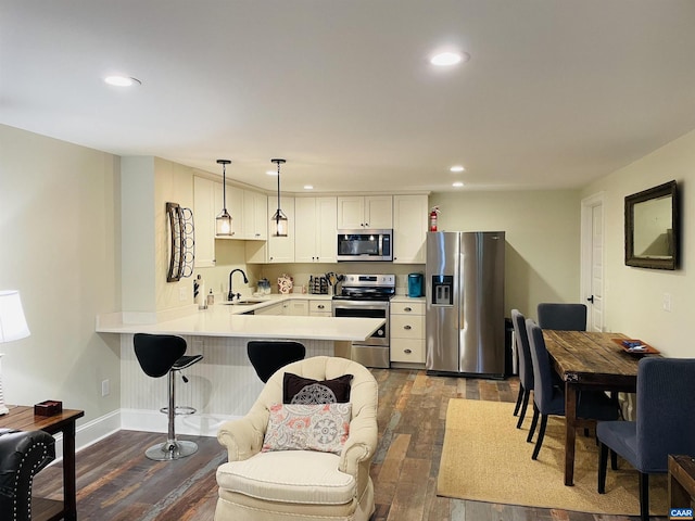 kitchen featuring a sink, dark wood-style floors, stainless steel appliances, a peninsula, and light countertops