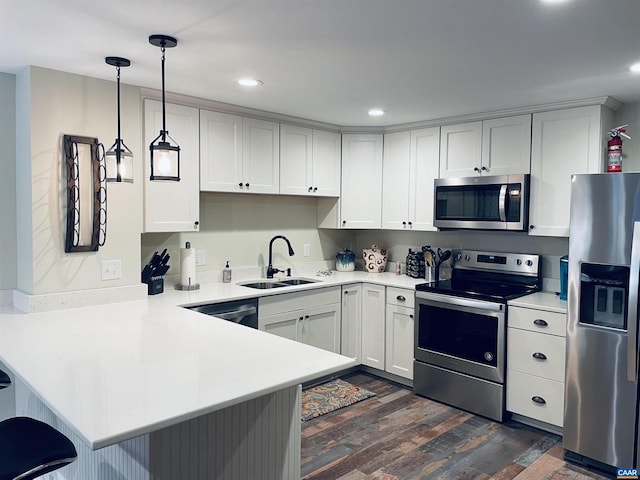 kitchen featuring a sink, dark wood-style floors, stainless steel appliances, a peninsula, and light countertops