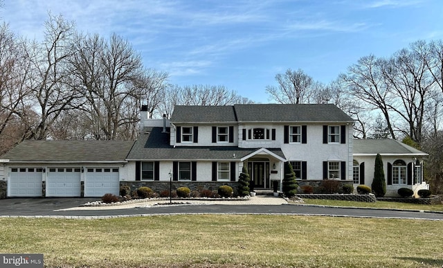 view of front of property featuring driveway, an attached garage, a chimney, and a front yard