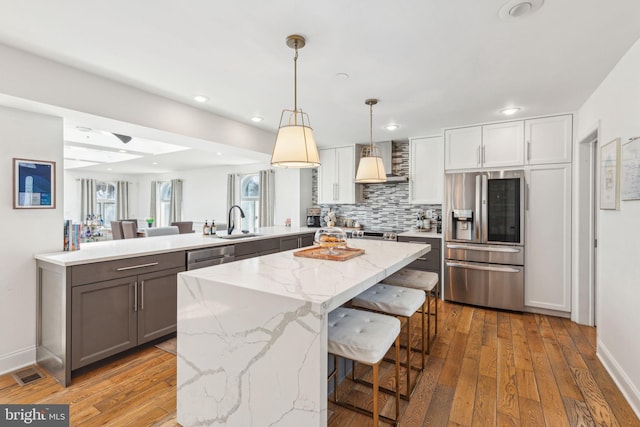 kitchen with light stone counters, a peninsula, a sink, stainless steel appliances, and wall chimney exhaust hood