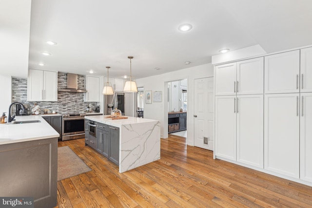 kitchen featuring stainless steel appliances, a sink, light wood-style floors, wall chimney exhaust hood, and tasteful backsplash