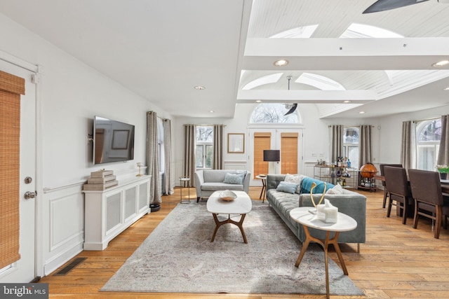 living area featuring lofted ceiling with skylight, light wood-style flooring, and a healthy amount of sunlight