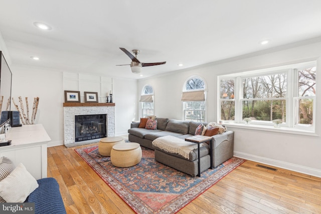 living room featuring visible vents, a stone fireplace, light wood-type flooring, and baseboards