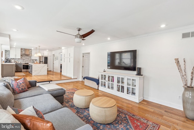 living room featuring visible vents, light wood-type flooring, ornamental molding, recessed lighting, and a ceiling fan