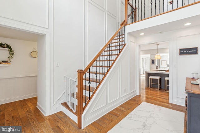 stairs with a decorative wall, recessed lighting, wood finished floors, and baseboards