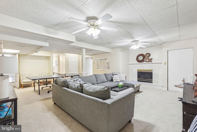 living area featuring a ceiling fan, a tile fireplace, a drop ceiling, and light carpet