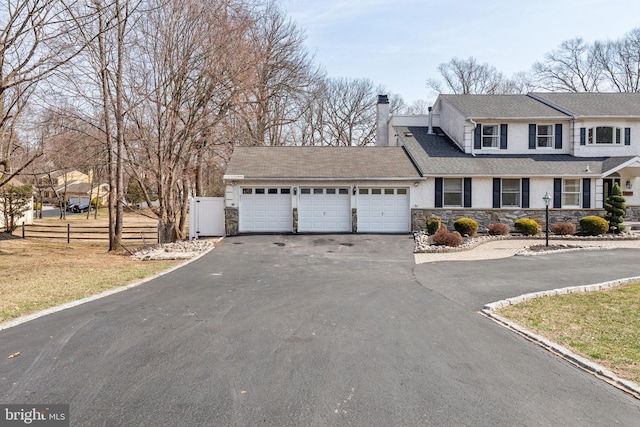 view of front facade featuring aphalt driveway, stone siding, fence, a garage, and a chimney