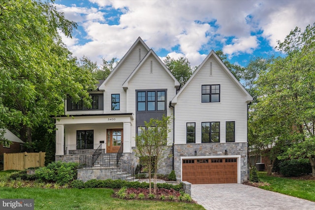 view of front of home with decorative driveway, stone siding, central AC, covered porch, and a garage