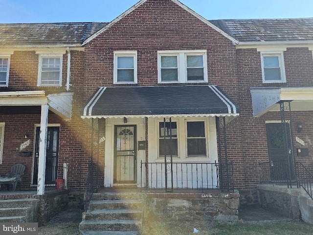 townhome / multi-family property with a high end roof, brick siding, and covered porch